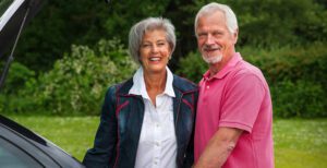 Older couple standing behind their car smiling.